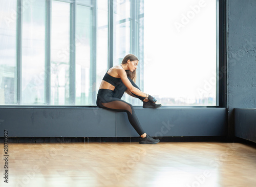 sporty woman tying shoelace while sitting on window seat in loft gym