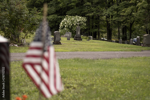 Cemetery graveyard with headstones, amaerican flag, grass and road during a cloudy day. photo