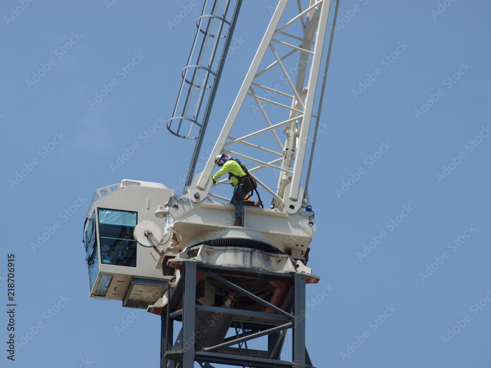 A worker with very visible safety harness stands on the gear table to loosen the first two bolts holding the tower boom.