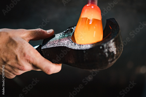 A glassmaker shapes an orb of molten glass in a wooden mold