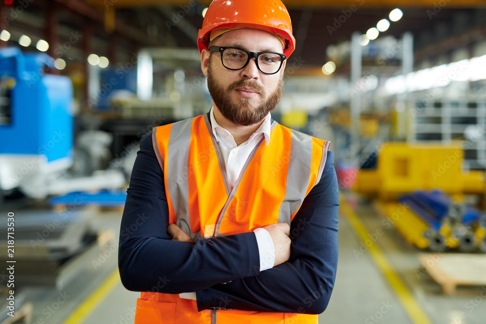 Waist up portrait of modern bearded businessman wearing hardhat and reflective vest looking at camera while posing confidently in production workshop, copy space Waist up portrait of modern bearded businessman wearing hardhat and reflective vest looking at camera while posing confidently in production workshop, copy space