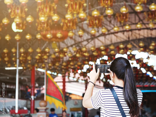 Back view of Asian girl taking photograph the lamp from mobile phone at China shrine. Chinese new year festival background.