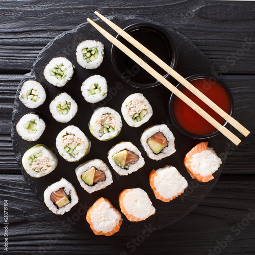 Menu set of Japanese rolls with salmon, tuna, avocado, cucumber served with sauces close-up on a stone. top view