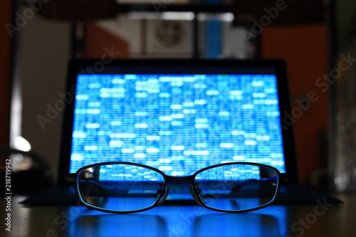 Glasses in front of laptop monitor. digital screen displayed blue light code blocks. computer language coding development concept. back of the house big data work environment. 