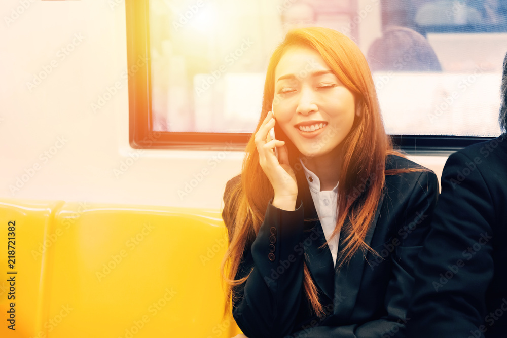 Happy smiling Asian businesswoman talking on the phone commuting on sky train.