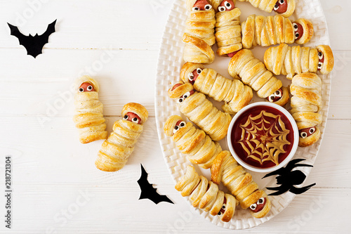 Scary sausage mummies in dough with funny eyes on table.  Halloween food. Top view. Flat lay. Banner