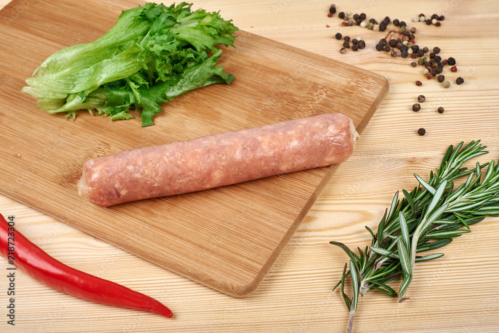 Raw sausages with vegetables and spices on wooden background