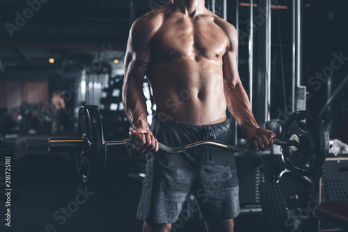 Shredded athlete is doing biceps curls with weight. He is standing and lifting equipment. Guy is spending active time in gym