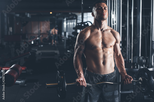 Fotografia Serious shirtless sportsman is doing biceps curls while using weight