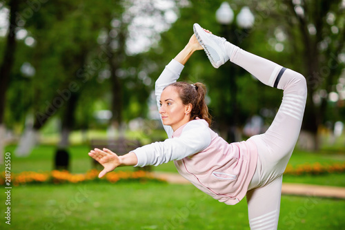 Young girl is making stretching fitness exercise outdoors standing on one leg. Concept of woman health