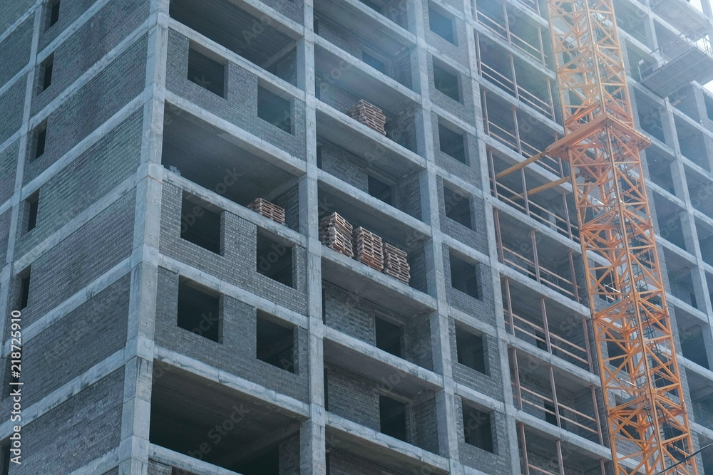 Multi-storey under construction building and construction crane on the background of clear sky. Close-up. Multi-storey under construction building and construction crane on the background of clear sky. Close-up.