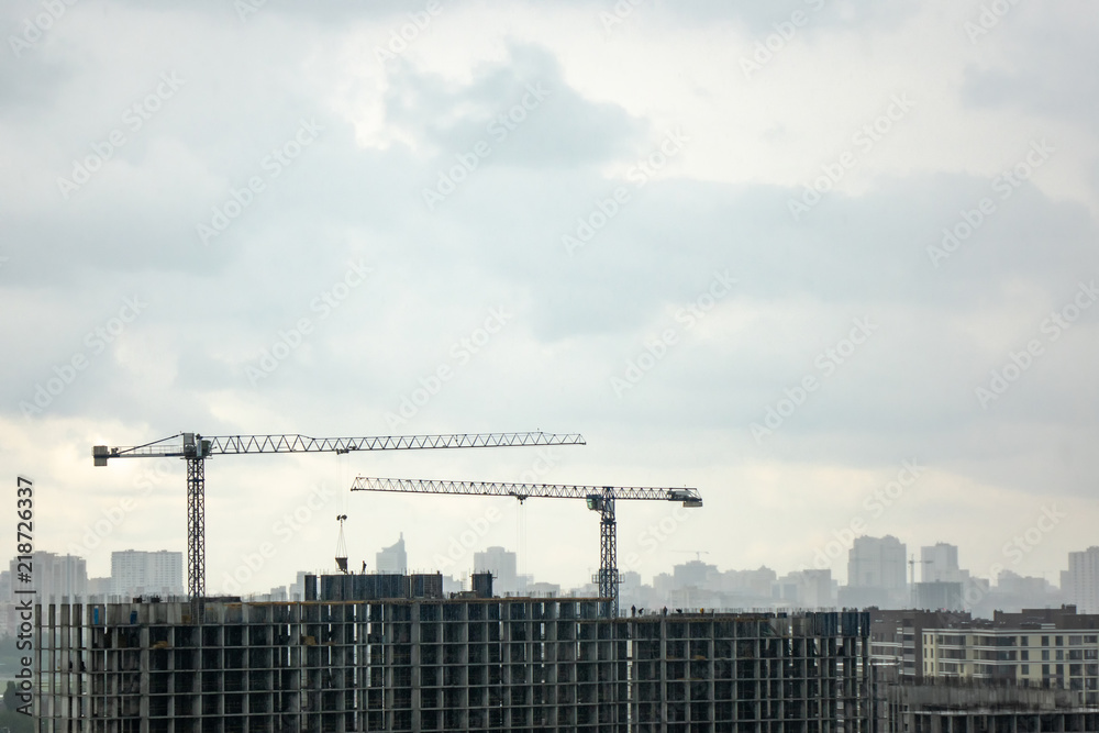 Building under construction with two tower cranes against a gray cloudy sky. Photo from the drone.