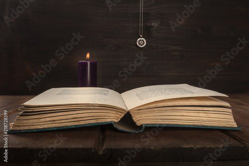 An open old book on a dark background with a burning candle, a pentacle, and copy space