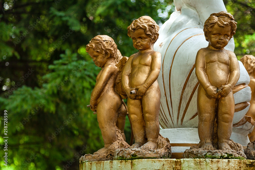 Close-up of three little angel boys statues, covered with bronze stand on a fountain in the city park