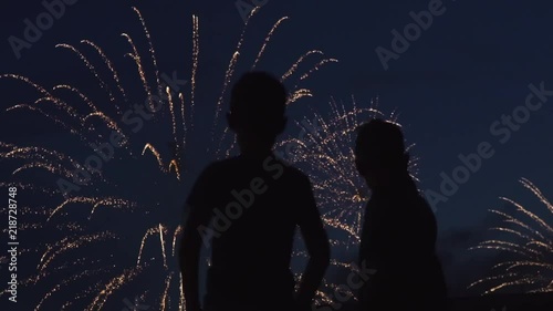 Silhouette of boys who watch the fireworks in the night sky. Bright and colorful lights in the sky. A beautiful sight is watched by the guys. Red, green and orange lights in the blue sky