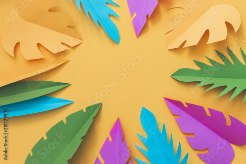 Colorful tropical palm leaves made of paper on orange background. Homemade craft. Summer concept. Empty space in the middle
