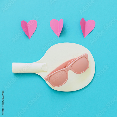 Pink sunglasses lies on a tennis racket with hearts. Summer sports love. Minimal concept.