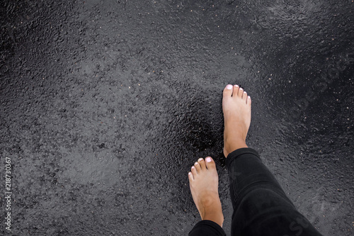 Young woman's barefoot walking on the wet, dark black asphalt after warm rain. Cloudy day in summer. Top view. Empty place for text. photo