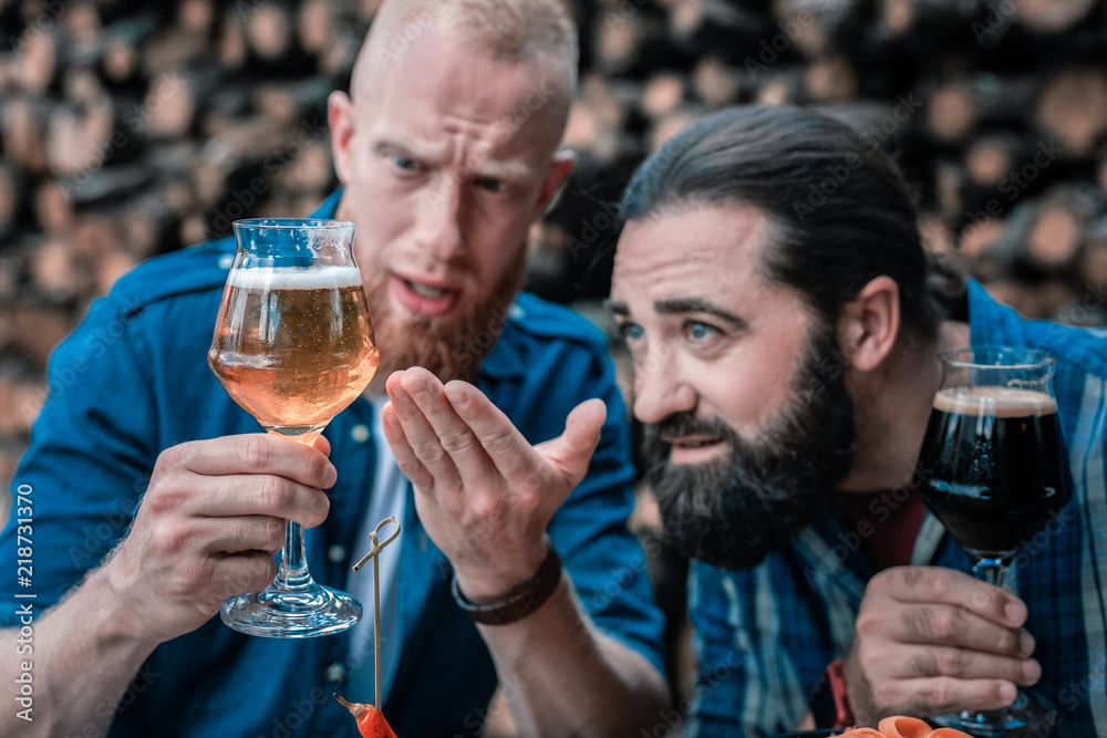 Light craft beer. Two bearded men looking at new type of light craft beer while sitting on nice summer terrace