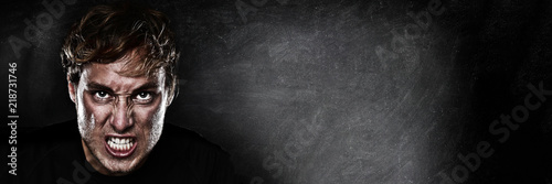 Angry agressive man face ready to fight on blackboard chalk board black texture background panoramic banner for advertising. Scary upset athlete focused to win.