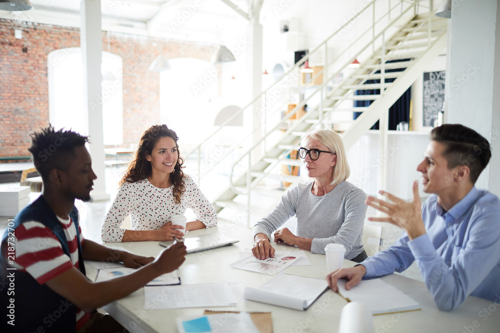 Group of business people gathered together at a table discussing an interesting idea at office Group of business people gathered together at a table discussing an interesting idea at office