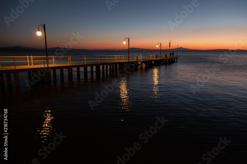 Some people on a pier at Trasimeno lake  Umbria  Italy  at dusk  with beautiful water reflections and warm colors