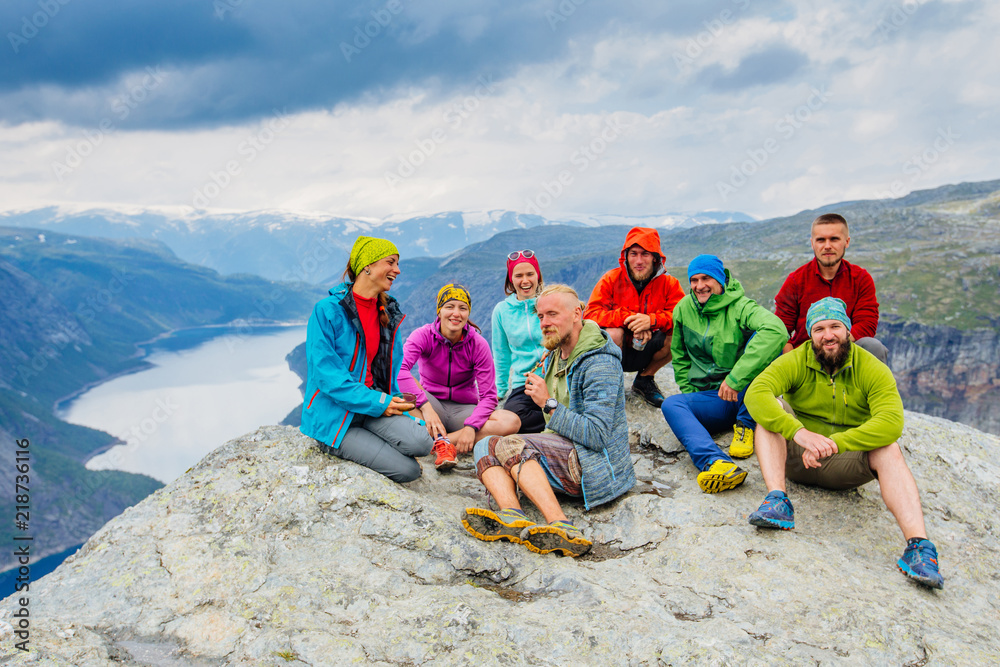 Happy young sportive people group of eight in bright colorful sportswear have fun and enjoy fresh air after hiking at beautiful summer day at Trolltinga Norway mountain. Full body portrait Happy young sportive people group of eight in bright colorful sportswear have fun and enjoy fresh air after hiking at beautiful summer day at Trolltinga Norway mountain. Full body portrait