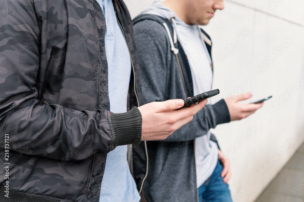 two antisocial mobile phone addicted male teenagers using smartphone, technology concept, leaning against wall with copy space two antisocial mobile phone addicted male teenagers using smartphone, technology concept, leaning against wall with copy space