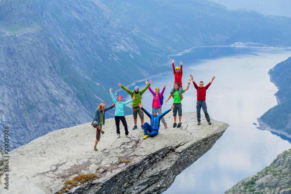 Happy young sportive people group of eight in bright colorful sportswear have fun and enjoy in Trolltinga Norway mountain. Full body portrait - obrazy, fototapety, plakaty 