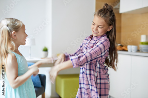 Two little sisters holding by hands and whirling in living-room while having fun