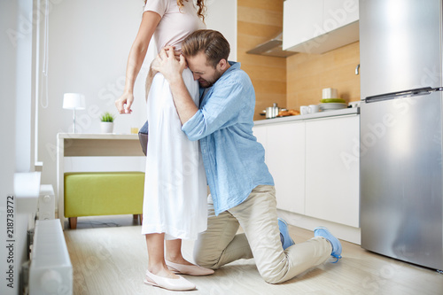 Young knelt apologizing man embracing his wife and begging her not to leave photo