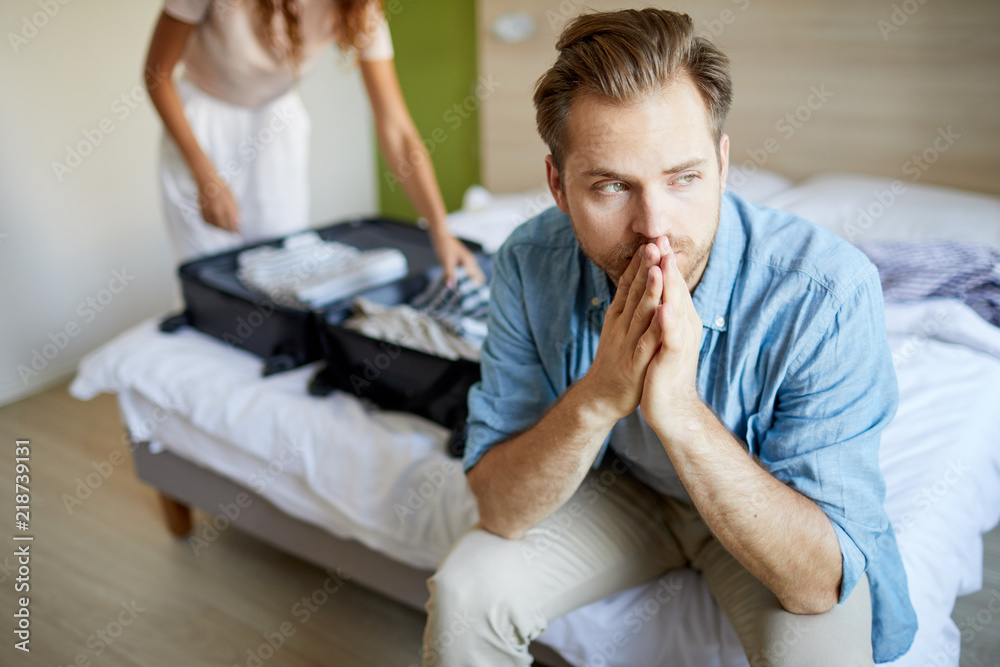 Sad Young Man Sitting On Bed And Thinking Of What To Do While His Wife Going To Leave Stock