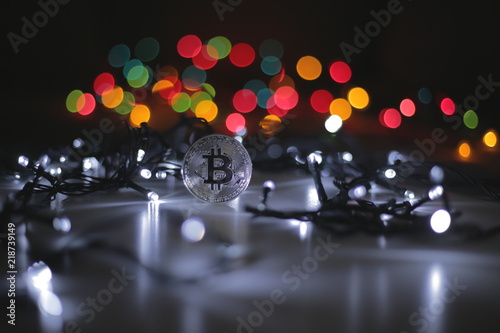 Coin of bitcoin payment system with decentralisation and electronic wallet. Festive atmosphere. Cold white Christmas tree lights in the background. BTC is a cryptocurrency. 4K, Panning, Closeup photo