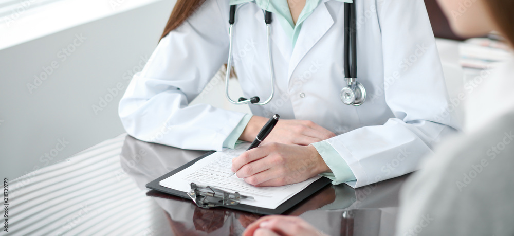 Doctor and patient in hospital. Physician filling up medication history records while talking with young woman. Healthcare and medicine concept Doctor and patient in hospital. Physician filling up medication history records while talking with young woman. Healthcare and medicine concept