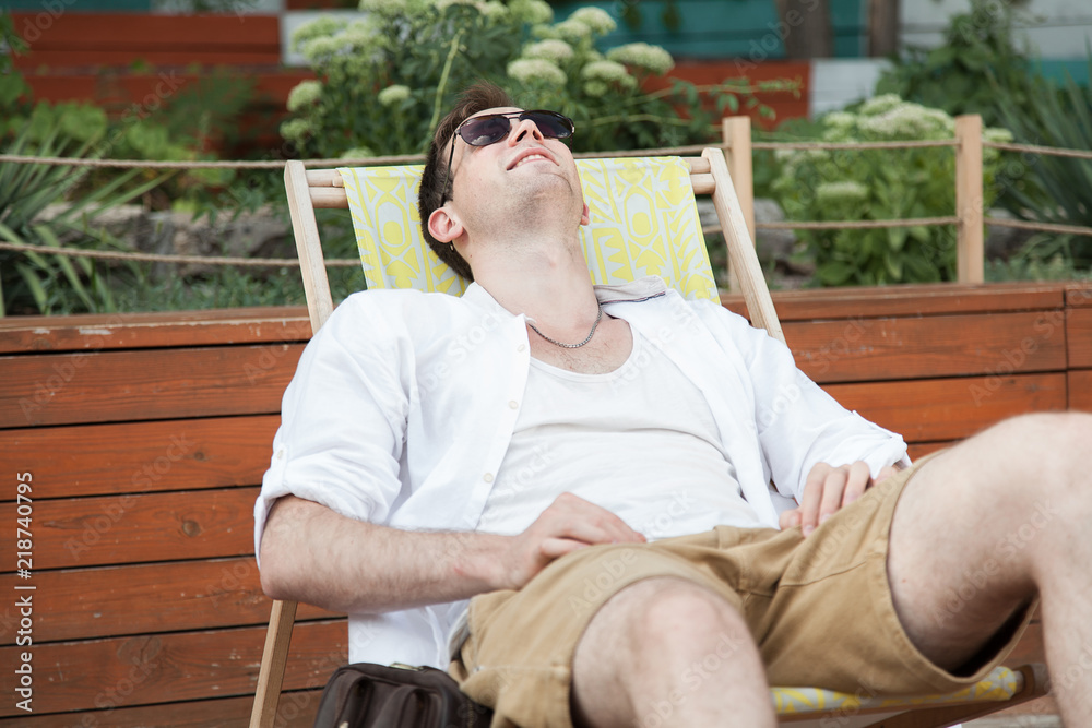 Obraz premium A young guy is sitting resting on a deckchair in the fresh air. Portrait.