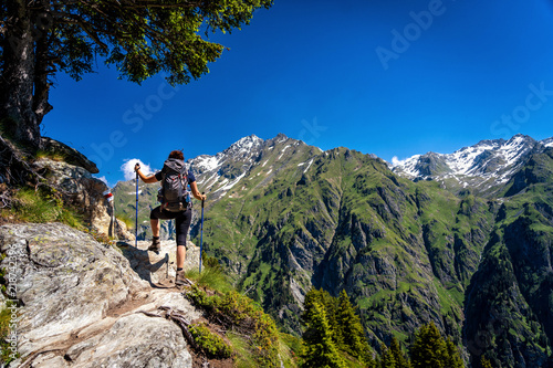 Female traveler with backpack hiking mountain trail and admiring views of Swiss Alps in Val de Bagnes area, Switzerland.