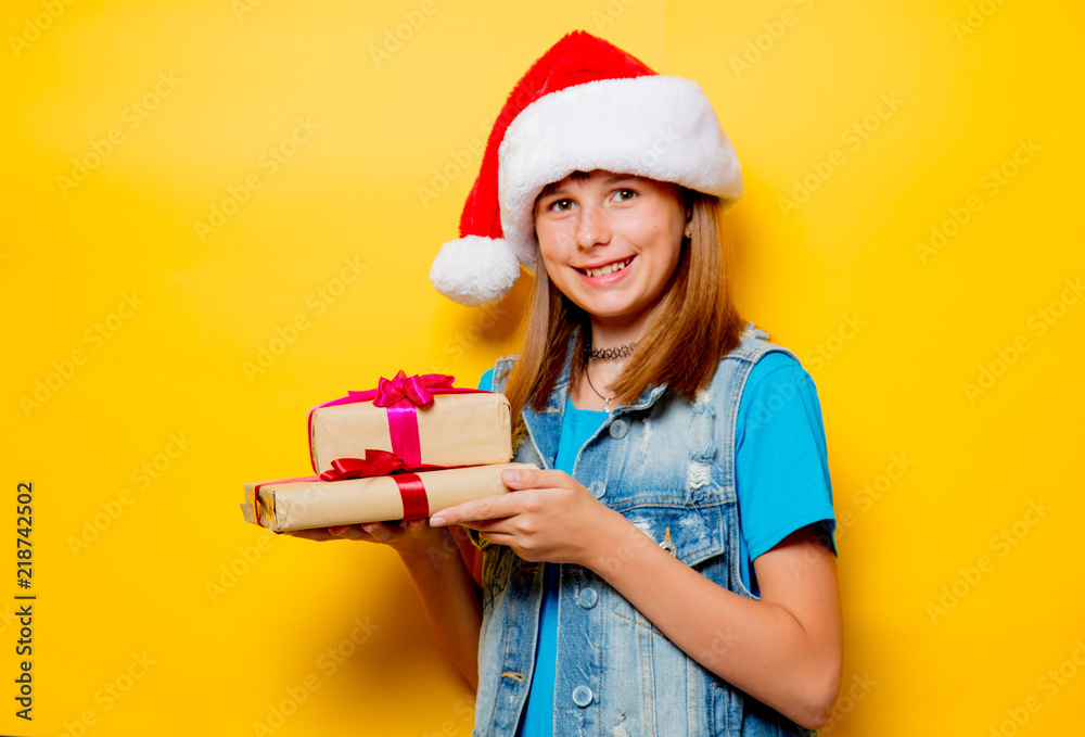 portrait of young teenage girl in Christmas hat with gift box on yellow background portrait of young teenage girl in Christmas hat with gift box on yellow background