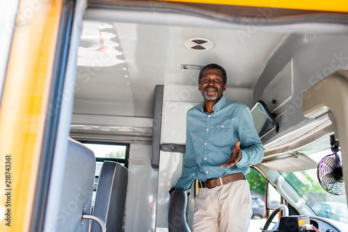 happy mature african american bus driver standing inside bus and looking at camera