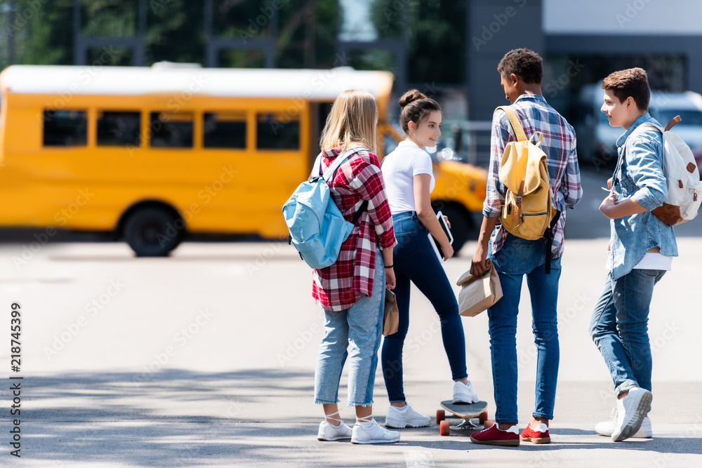 Group of teen scholars spending time together on parking in front of school bus