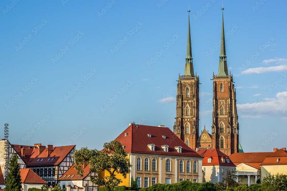 Naklejka premium medieval old city street view with red roofs of small house and gothic tower of catholic church on blue sky background in colorful summer bright contrast day time