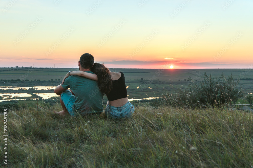 Fototapeta premium Couple is hugging and sitting close on a hill at sunset