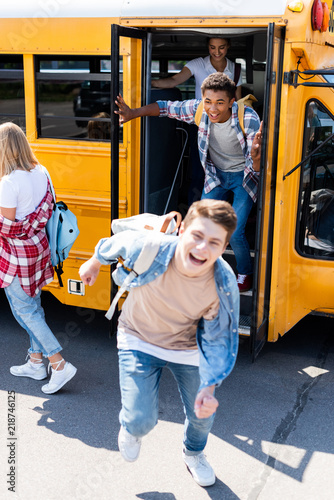 group of joyful teen scholars running at school from bus