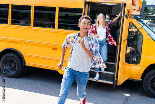 multiethnic teen students couple running out of school bus