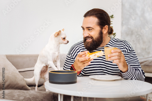 Cheesecake and latte. Bearded man eating cheesecake and drinking latte while looking at his little cute dog