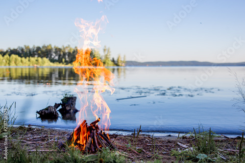 Beautiful campfire in the evening at lake. Fire burning in dusk at campsite photo
