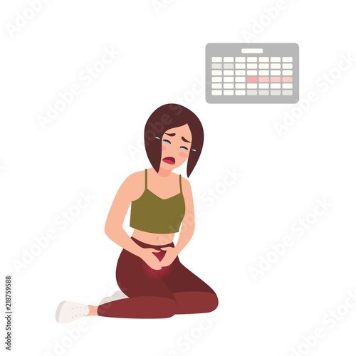 Young woman suffering from painful menstruation against calendar hanging on w...