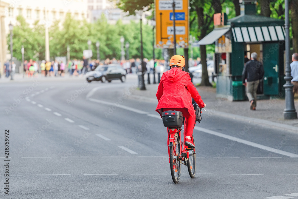 woman in red rides a bike at city street, view from the back