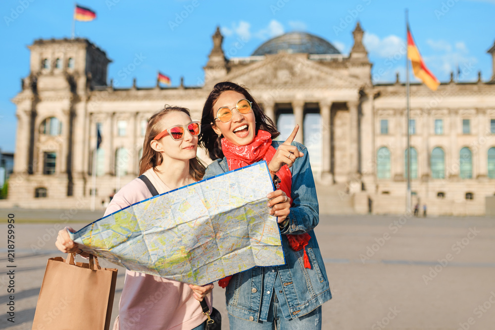 Naklejka premium Wielorasowa grupa przyjaciół odwiedzających Berlin. Dwa kobiety czyta mapę z Reichstag budynkiem na tle. Koncepcja przyjaźni i podróży z prawdziwymi szczerymi emocjami