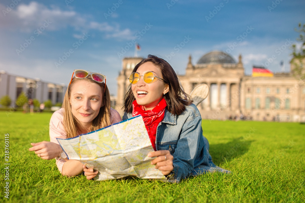 Fototapeta premium Multiracial group of friends visiting the city of Berlin. Two women reading map with Reichstag building on the background. Friendship and travel concept with real candid emotions