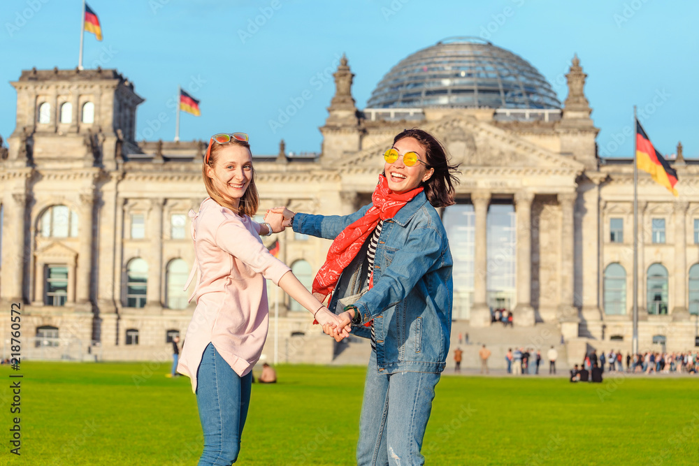 Naklejka premium Dwa młodej studenckiej dziewczyny ma zabawę, tana i piggybacking na trawie blisko sławnego punktu zwrotnego w Berlin - Bundestag budynek. Koncepcja podróży